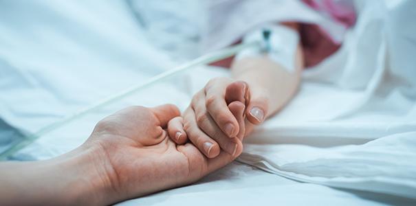 Parent holding kid's hand in hospital bed